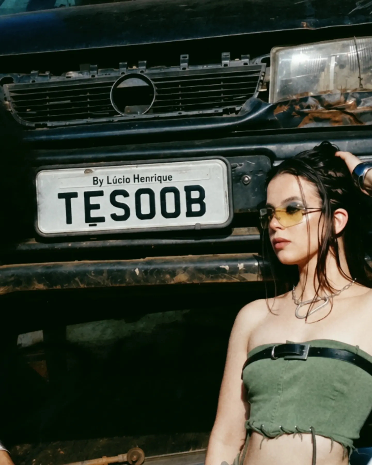 Modelo usando o look verde junto ao carro com a placa Tesoob.